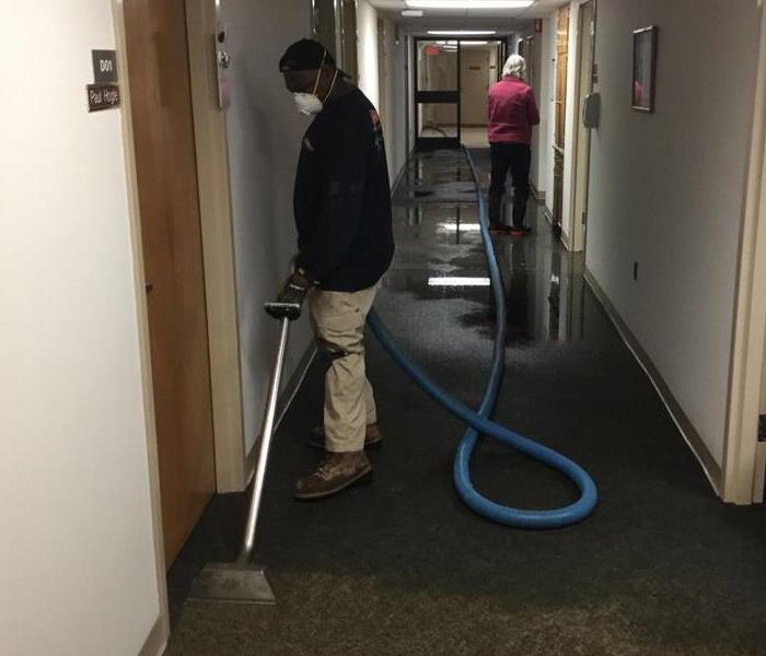 hallway with wet carpet and male employee vacuuming 