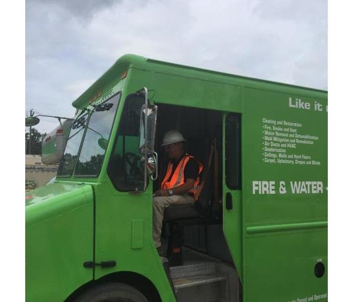 green SERVPRO box can with a man in the driver seat wearing an orange vest and white hard hat.